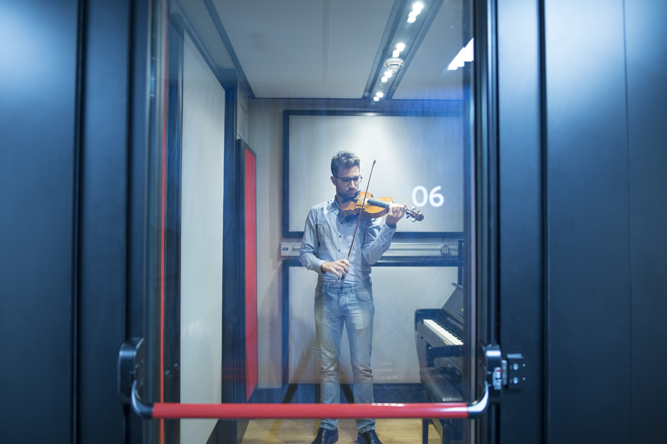 A male student practising on the violin, in a solo practise pod, at the RCM.